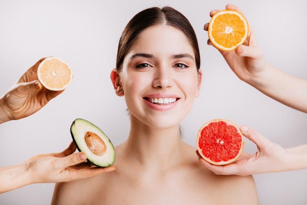 A person is surrounded by fresh citrus fruits and an avocado, symbolizing a healthy skincare or beauty routine.