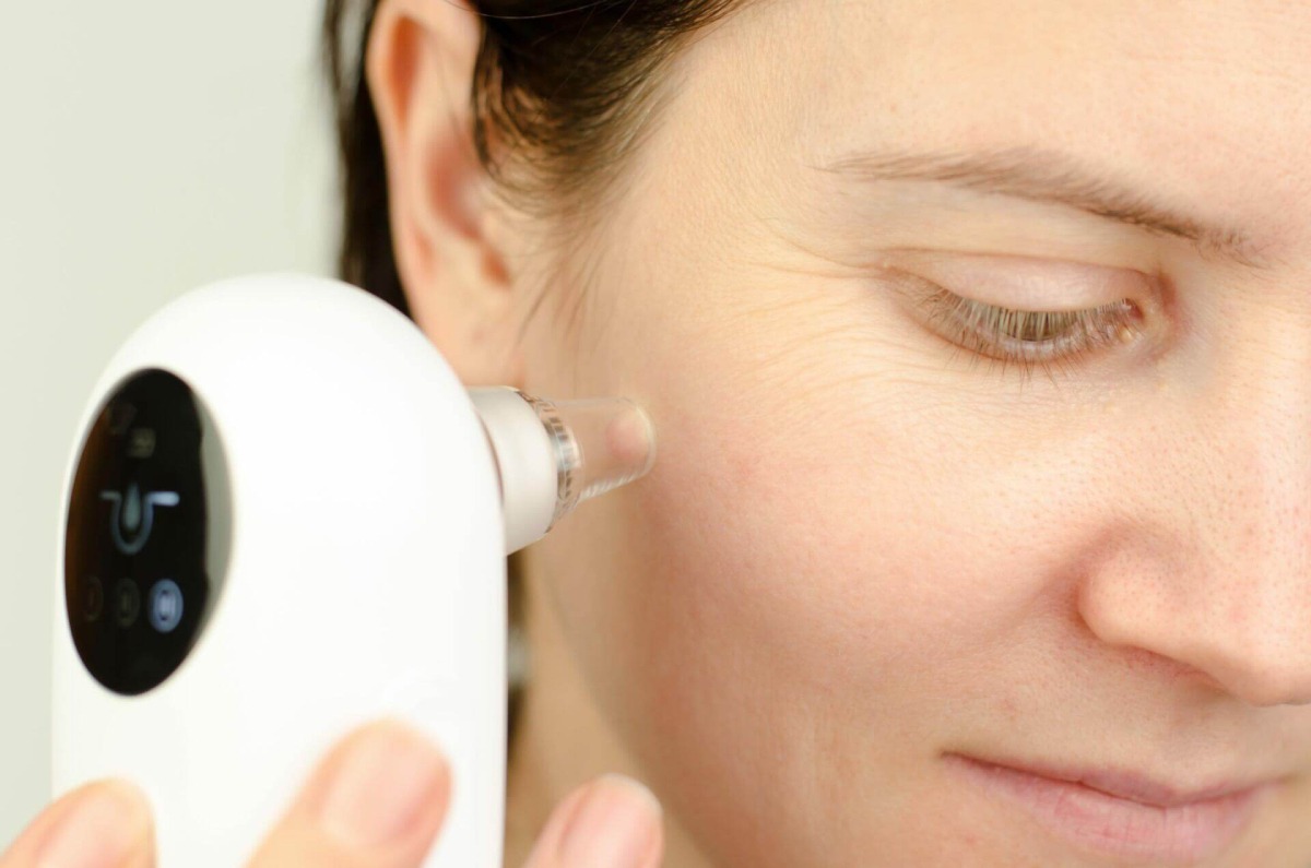 A person holds a white skincare device near their ear, showcasing its sleek design and digital interface.