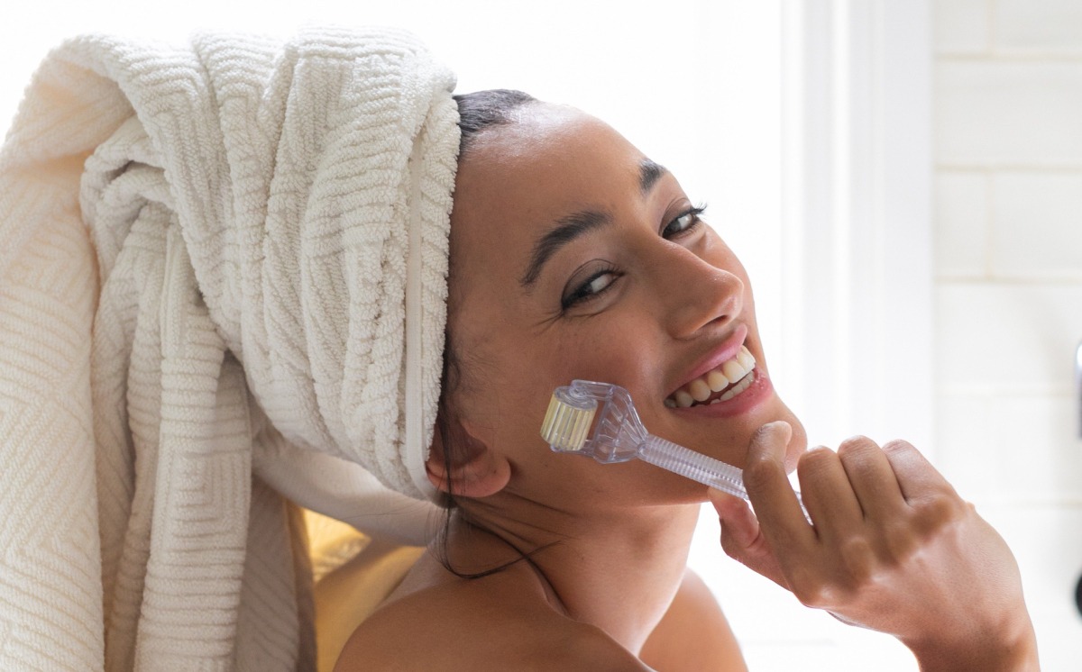 A woman sitting in a bright bathroom, wrapped in a white towel, thoughtfully resting her chin on her hand.