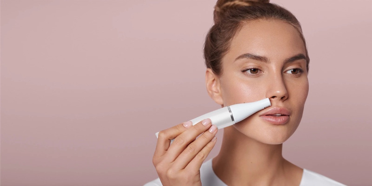 A woman holds a skincare product near her face, set against a soft pink background, with a focus on her hands and the product.