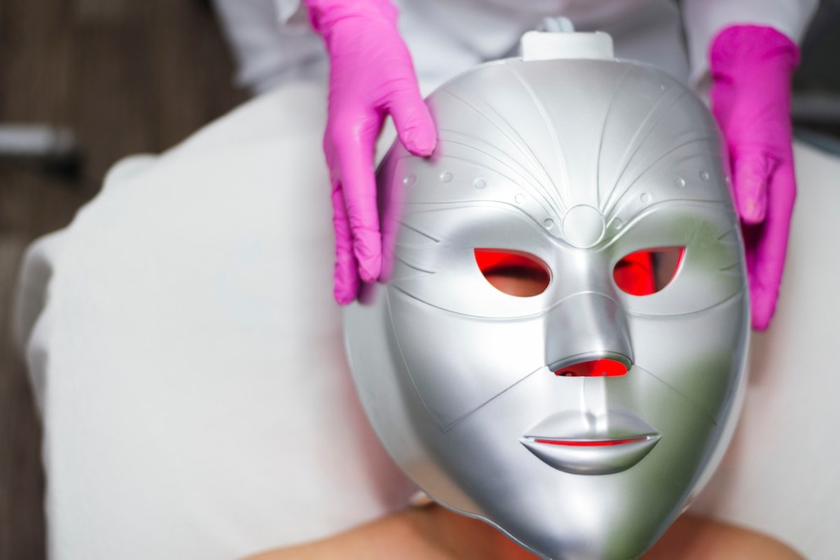A person receives a skincare treatment, with a technician wearing pink gloves holding a treatment device above their face.