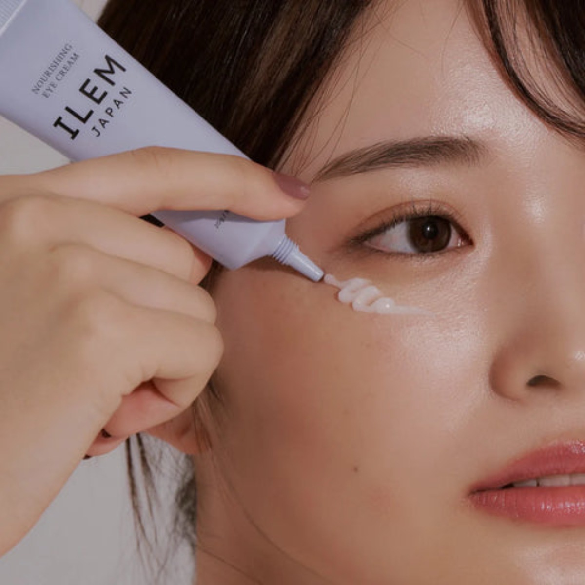 A hand holds a tube of ILEM nourishing cream, showcasing its sleek design against a neutral background.
