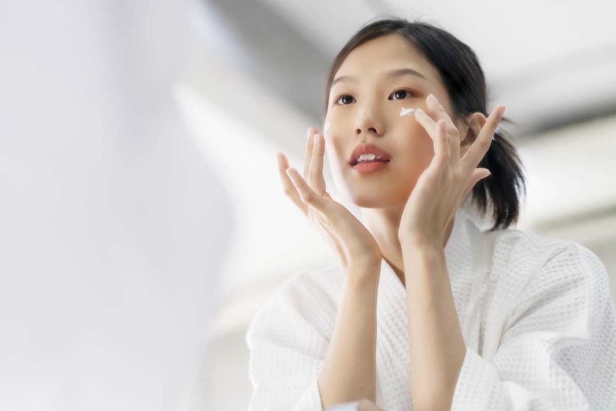 A person in a white robe is touching their face, set against a softly blurred, bright background, suggesting a moment of relaxation.