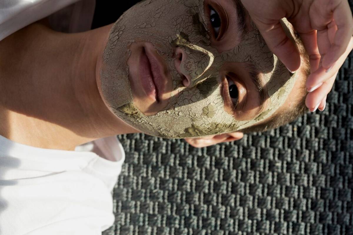 Person holding a peeled-off dry clay mask in front of their face, revealing part of their natural skin underneath.