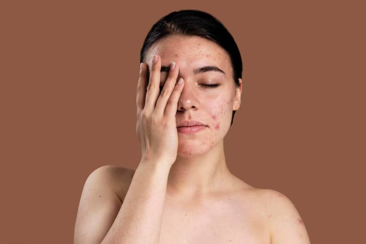 A person with long dark hair is partially covering their face with one hand, against a solid brown background.