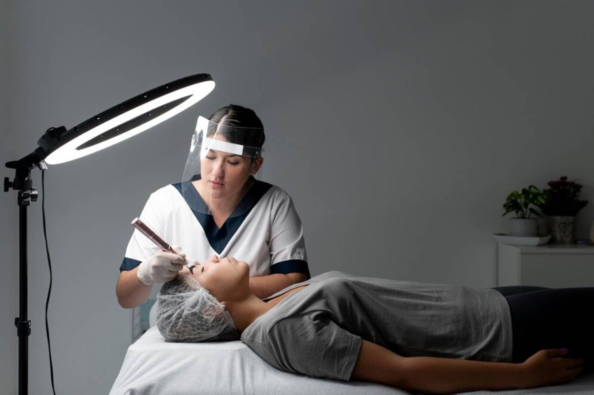 A professional applies a beauty treatment to a client under a bright ring light in a serene treatment room.